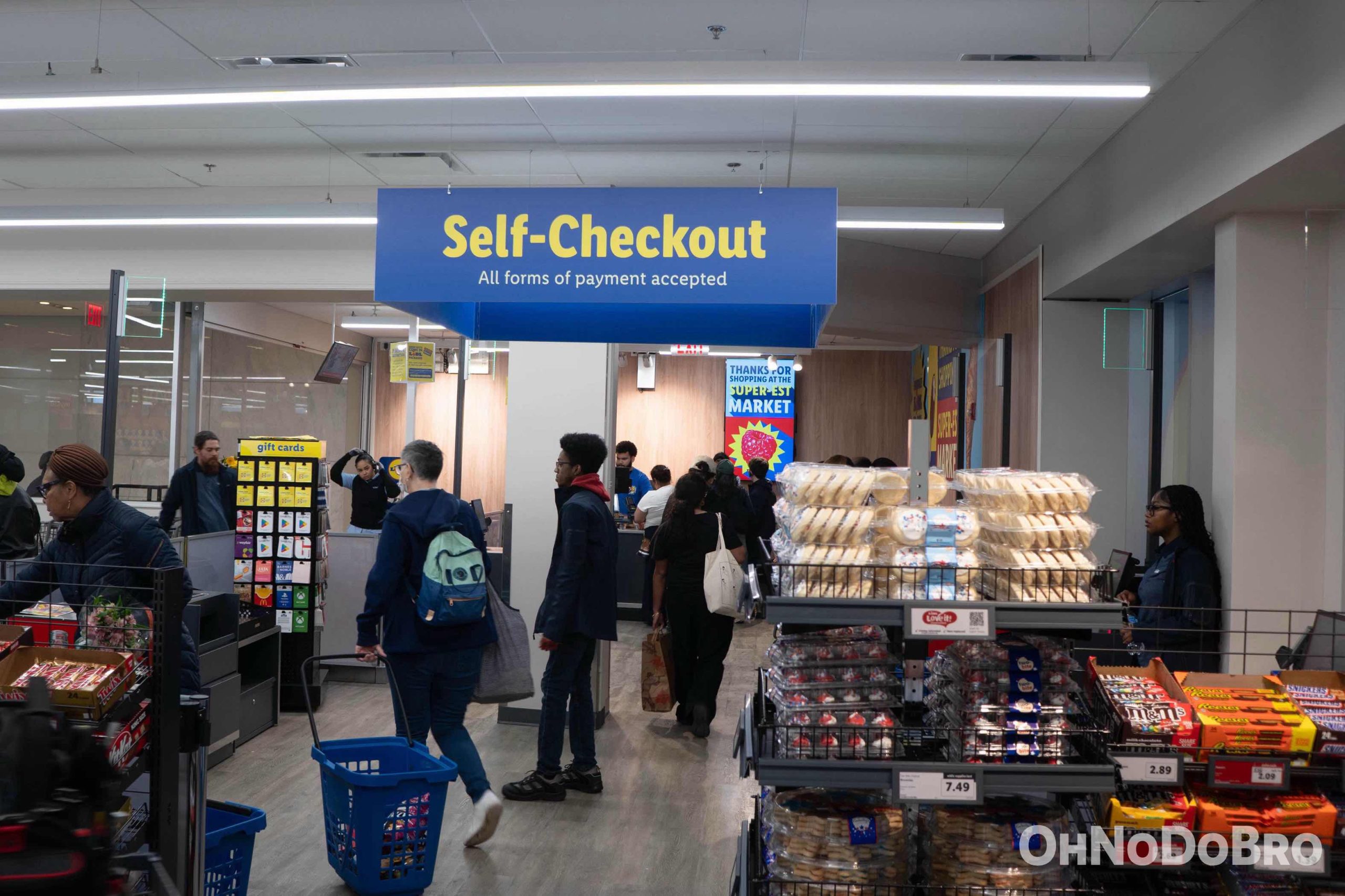 The Self-Checkout section of the store. Custmers are checking out and a sign above denotes the section of the store